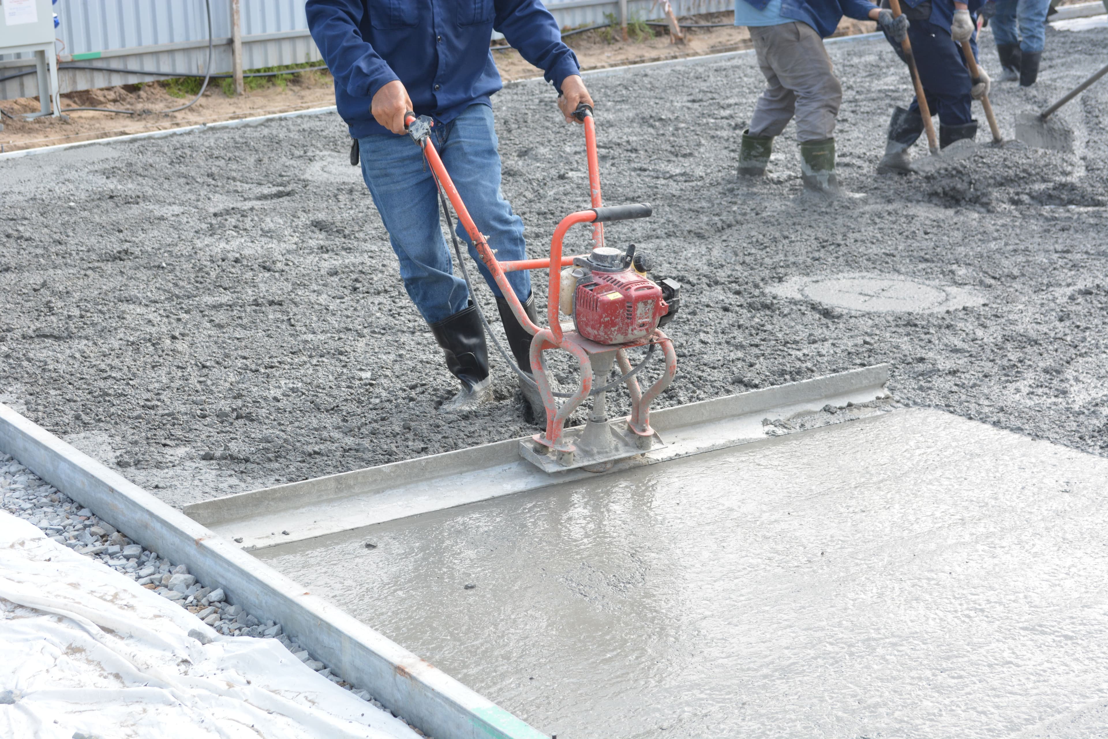 A contractor finishing a freshly poured concrete slab on a job site